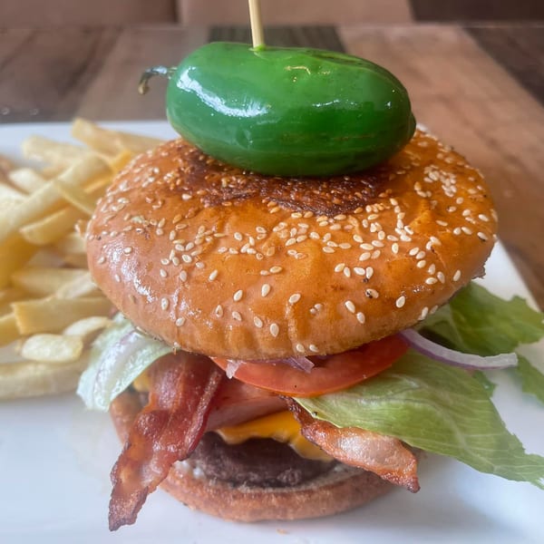 A Don Tequila Bar & Grill burger with bacon, cheese, lettuce, tomato, and a jalapeño on top, served with fries.