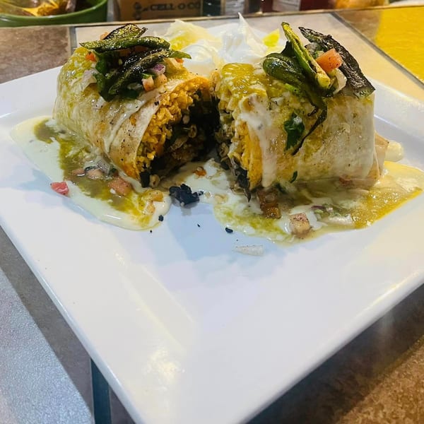 A large burrito, cut in half, covered in green sauce and sour cream on a white plate.