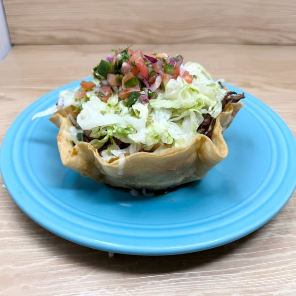 A taco salad in a crispy tortilla bowl, topped with lettuce, pico de gallo, and sour cream.